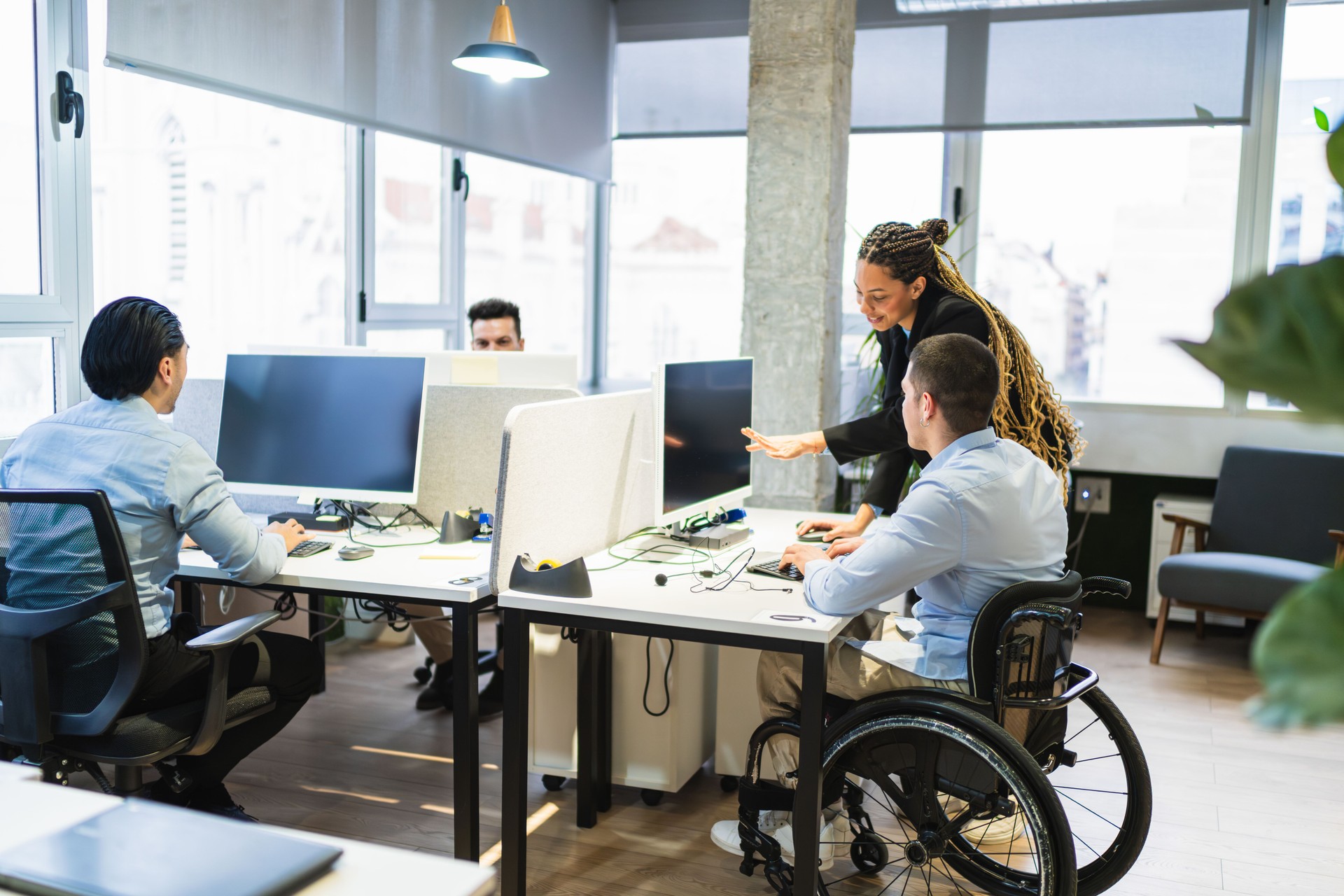Young professionals collaborating in modern coworking space with disabled colleague